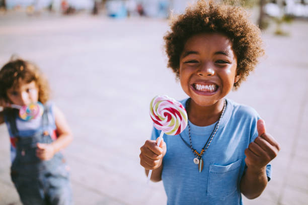 Multi-ethnic children with colorful lollipops outdoors on summer vacations Happy multi-ethnic mixed family little boys eating lollipops in summer in the city candy in mouth stock pictures, royalty-free photos & images