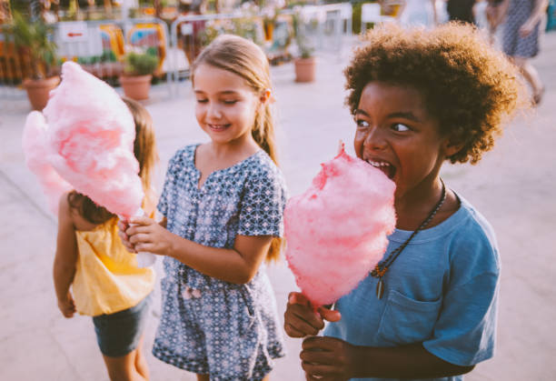 multi-etnische kindertjes suikerspin eten in pretpark - kermis stockfoto's en -beelden