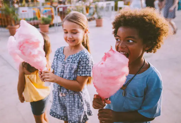 Happy multi-ethnic kids eating pink cotton candy at travelling carnival on summer holidays