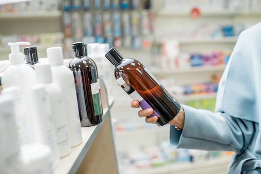 Woman taking a bottle with cosmetics from the shelf of the pharmacy supermarket, close-up view on the bottle with blank label