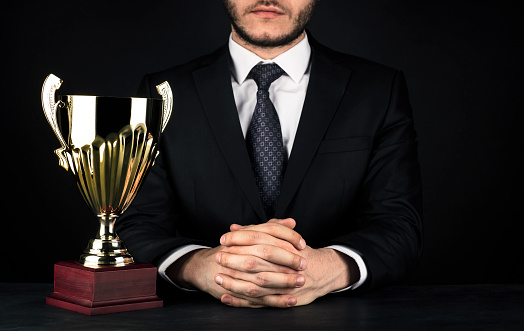 Young adult man holding a trophy. Low key.