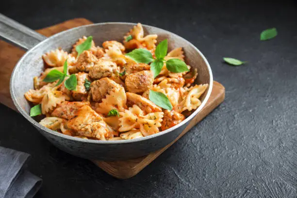 Farfalle pasta in tomato sauce with chicken,  basil in pan. Chicken italian bow tie pasta over concrete background with copy space, homemade italian food.