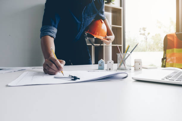 istock Hands of architect or engineer with helmet using pencil working with blueprint on desk in office . Engineering tools and construction concept. Architect and Business concept. 950310176