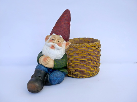 Sleeping, sitting garden gnome leans against a basket. Isolated on white background