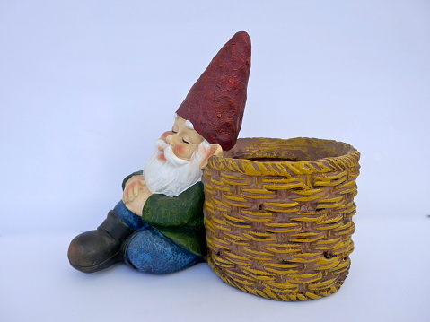 Sleeping, sitting garden gnome leans against a basket. Isolated on white background
