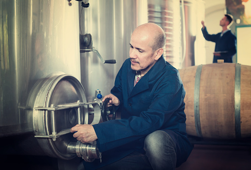 Smiling man machinery operator working on secondary fermentation equipment in winery manufactory