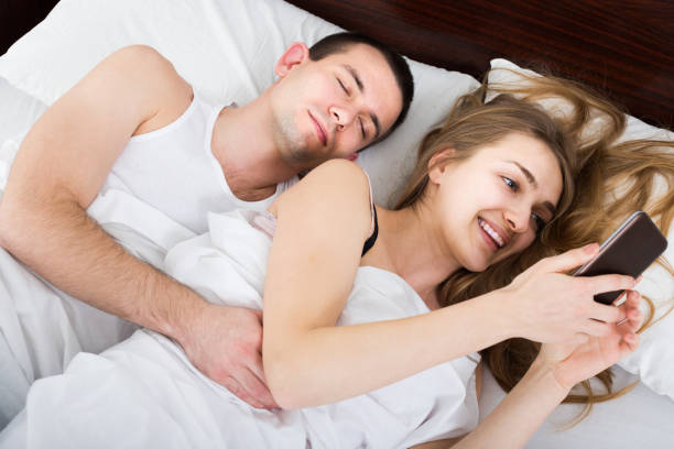 istock girl chatting with mobile, man sleeping by in bed 950324818