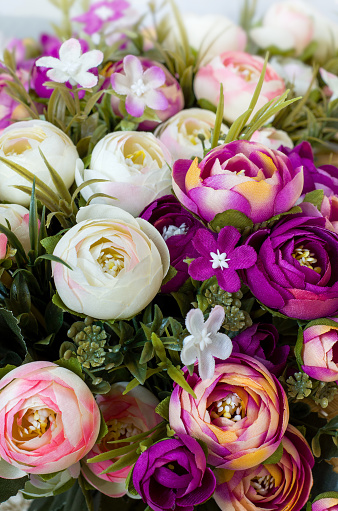 Still life with artificial flowers of roses and carnations in red, purple, yellow and white and green petals. The image is vertical, close-up.