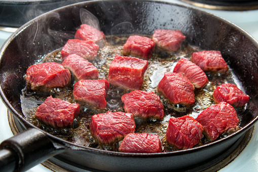 Searing beef bottom round roast cubes in cast iron skillet , closeup