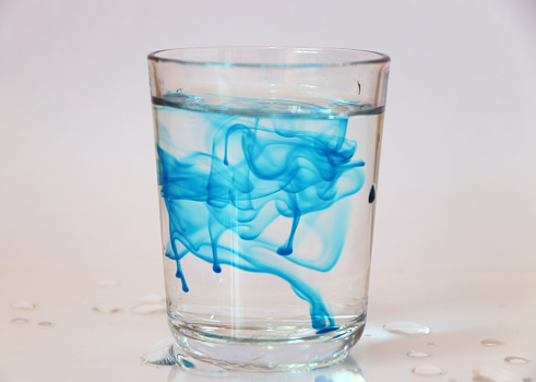Blue color free movement in a glass of water, on white background.