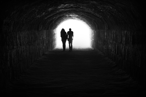 A businessman walks out of a tunnel as his silhouette is engulfed by a bright light.