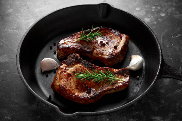 istock Cooked Pork Loin chops in rustic skillet, pan with rosemary. top view. background 950346142