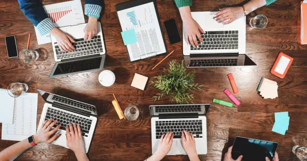 Photo of Top view of coworking people sitting together around table. Business meeting of young creative hipsters. Team of analysts make conversation about new project plan. Social content. Wide