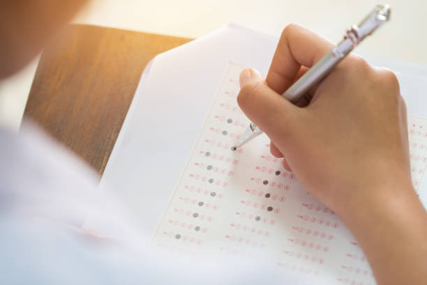 istock Education test concept : Hands student holding pen for testing exams writing answer sheet or exercise for taking fill in exam carbon paper computer on wood table at classroom in high school 950351530