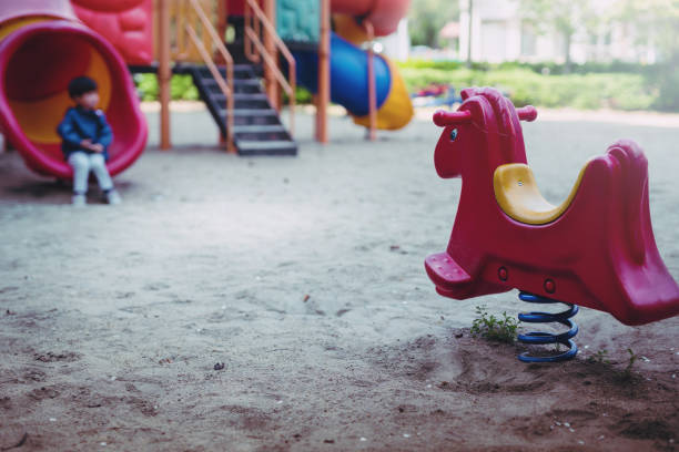 garotinho está jogando sozinho no parque infantil. garotinho está infeliz no playground. - sadness child little boys loneliness - fotografias e filmes do acervo