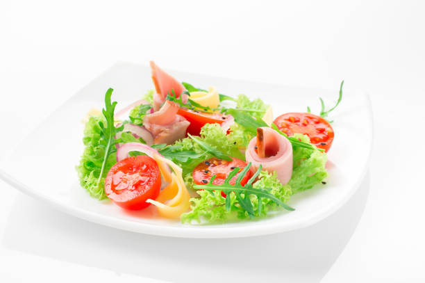 istock Fresh salad with tomatoes, arugula, cheese and ham on the white plate and white background 950355172