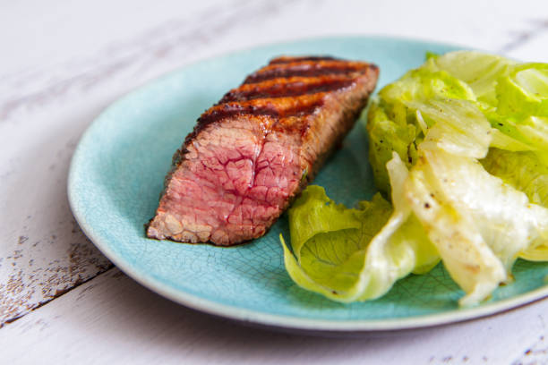 istock Fresh beef steak with lettuce leaves on a ceramic plate side view 950363262