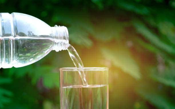 istock hand holding water glass and bottle in nature background. 950364384