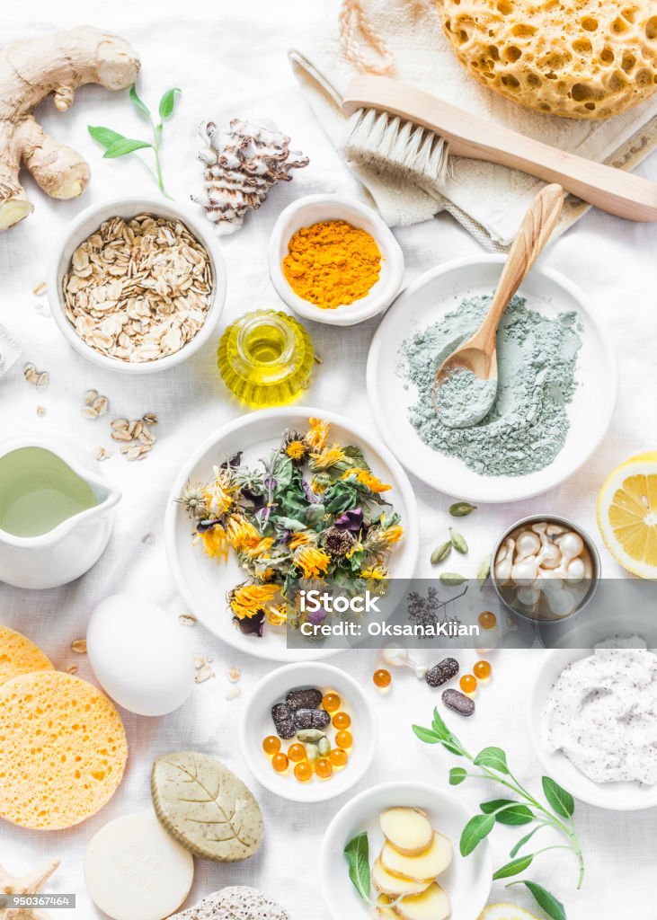 Home beauty products - clay, oatmeal, coconut oil, turmeric, lemon, scrub, dry flowers and herbs, sponges, soap, facial brush on light background, top view. Skin youthfulness, beauty concept. Flat lay Ingredient Stock Photo