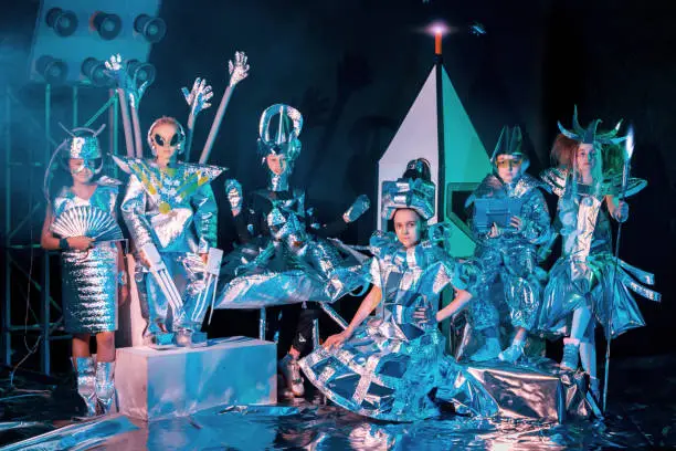 Group of children dressed in silver foil space costumes. The children elementary ages are posing together. They are looking at the camera. Studio shooting on black background with a spaceship