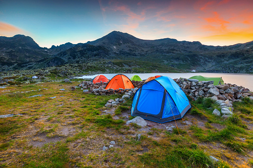 Amazing mountain camping place, colorful tents near Bucura alpine lake. Fantastic sunset in mountains with campground, Retezat mountains, Transylvania, Romania, Europe