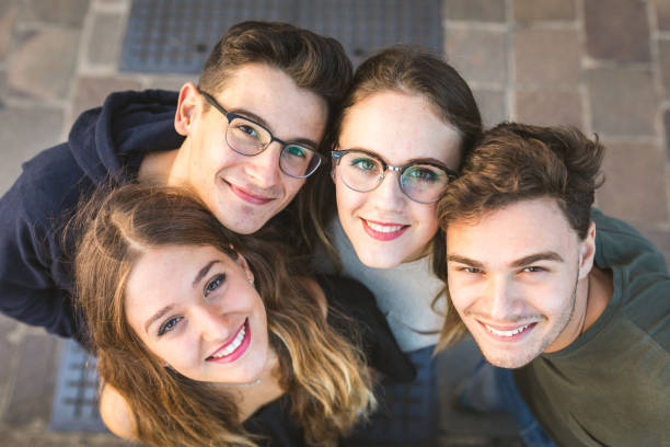 Teen friends portrait sitting together on a wall in the city Teen friends portrait sitting together on a wall in the city. Close view of two girls and two boys sitting together and embracing. Friendship and lifestyle concepts group of people wearing eyeglasses stock pictures, royalty-free photos & images