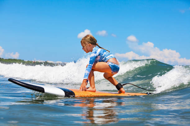 Young surfer rides on surfboard with fun on sea waves Happy baby girl - young surfer ride on surfboard with fun on sea waves. Active family lifestyle, kids outdoor water sport lessons and swimming activity in surf camp. Summer vacation with child. raro stock pictures, royalty-free photos & images