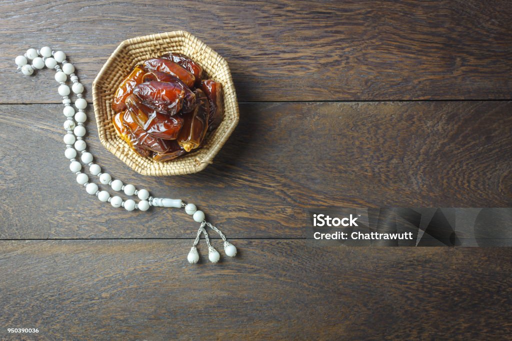 Table top view aerial image of decoration Ramadan Kareem holiday background.Flat lay date in wood basket with white prayer beads on modern rustic brown wood at office desk.Free space creative design text. Arabia Stock Photo