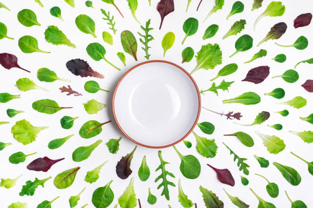 Different salad leaves and a bowl on white background