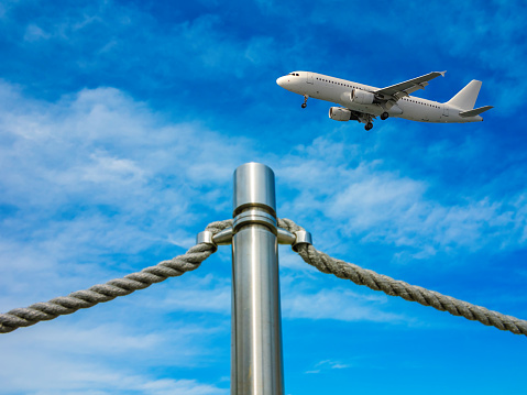 The barrier fence in the form of an iron pillar and ropes of the airport on blue sky background. Landing airplane.