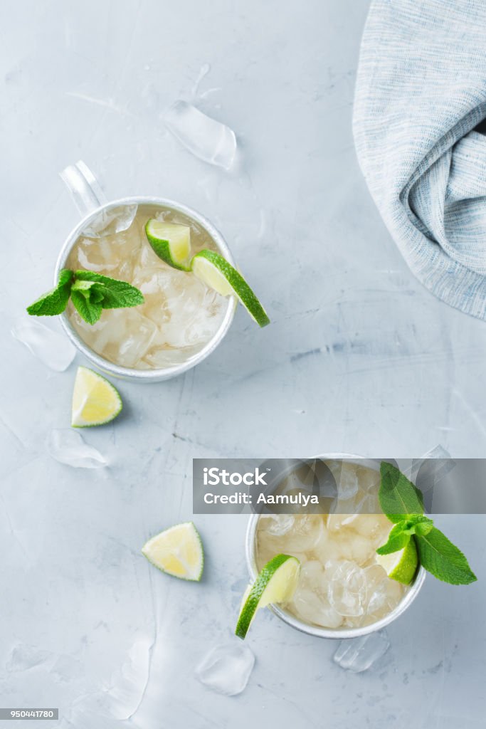 Moscow mule cocktail with vodka, ginger beer, lime and mint Food and drink, holidays party concept. Cold fresh classic alcohol beverage moscow mule cocktail in a silver mug with vodka, ginger beer. lime and mint for refreshment in summer days Top view flat lay Ale Stock Photo