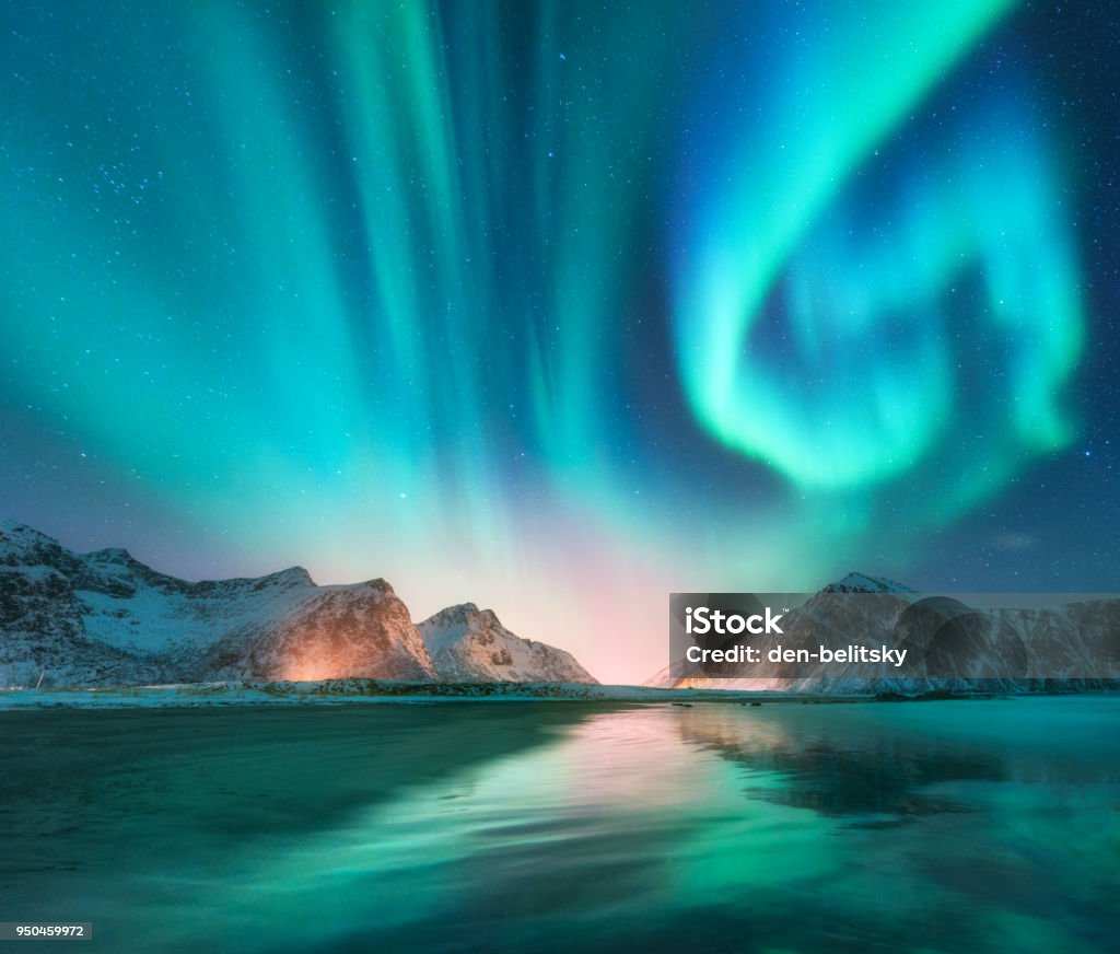 Aurora Boreal en las islas Lofoten, Noruega. Aurora. Aurora Boreal verde. Cielo estrellado con luces polares. Paisaje invernal de noche con la aurora, el mar con el reflejo del cielo, piedras, playa y montañas nevadas - Foto de stock de Fiordo libre de derechos