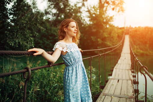 young beautiful girl standing on the bridge over the river. Redhead or blonde romantic waiting for a man. Maybe sad, fashion photography