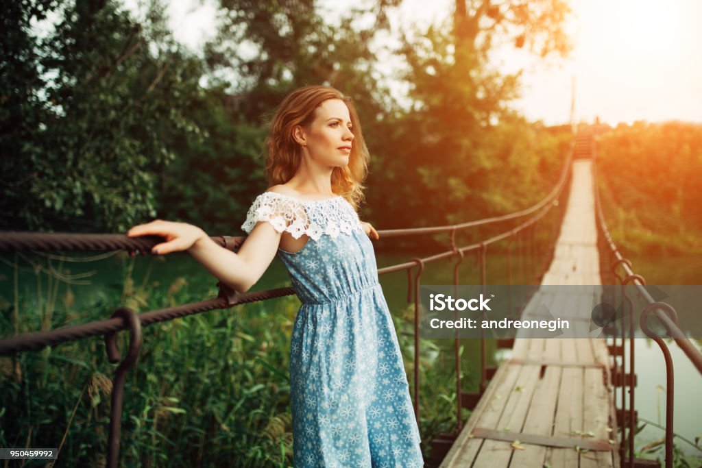 young beautiful girl standing on the bridge over the river. young beautiful girl standing on the bridge over the river. Redhead or blonde romantic waiting for a man. Maybe sad, fashion photography Bridge - Built Structure Stock Photo