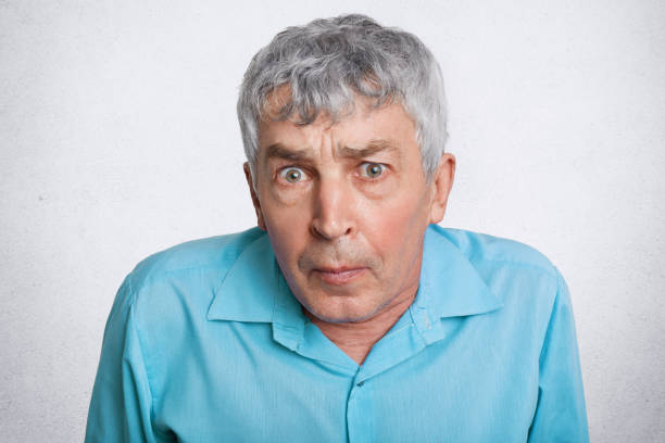 istock People, age and emotions concept. Surprised grey haired elderly man looks with unexpeted expression into camera, wears blue formal shirt, isolated over white background. Mature male poses indoor 950463298