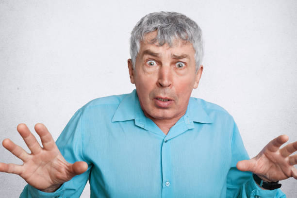 istock Scared matured wrinkled male expresses negative emotions, gestures and looks with unexpected expression into camera, wears formal shirt, isolated over white background. Facial expressions concept 950463314