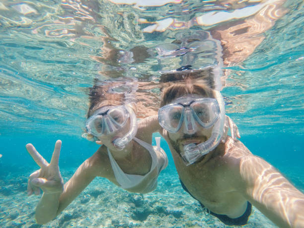 young man taking action camera selfie in crystal blue water, vacations summer concept - vacations couple travel destinations snorkeling imagens e fotografias de stock