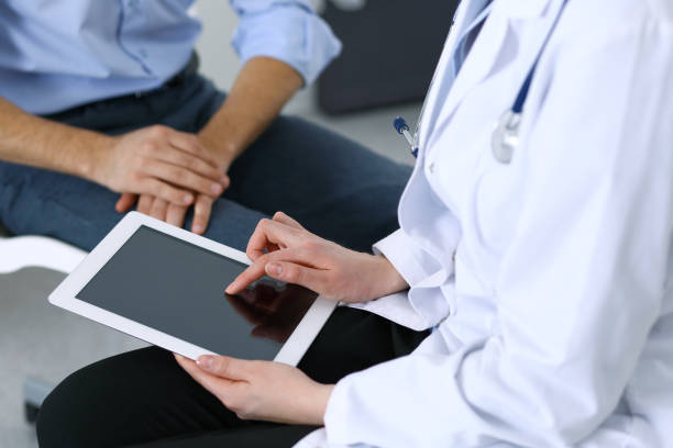 istock Female doctor using touchpad or tablet computer while consulting man patient in hospital. Medicine and healthcare concept 950486454