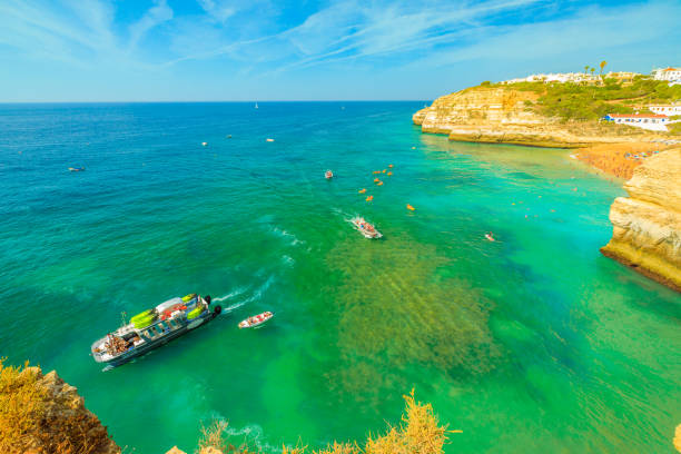 Benagil, Portugal - August 23, 2017: aerial view from promontory in Algarge Coast of boats and kayaking tour to famous sea cave Algar de Benagil. Praia de Benagil in the distance. Turquoise waters.