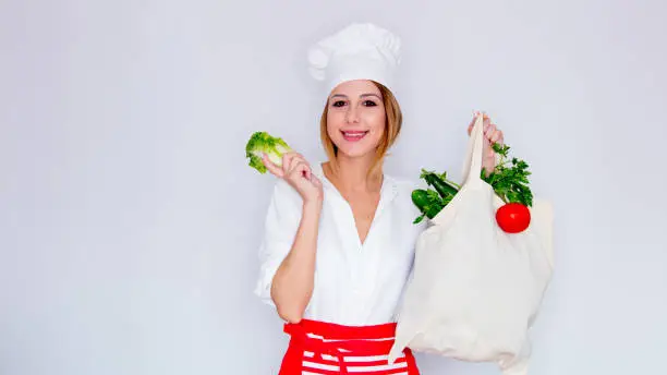 woman in cook uniform holding with different vegetables and showing salad leaves