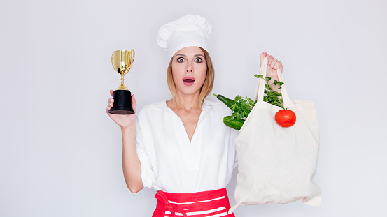 woman in cook uniform holding with different vegetables and prize cup