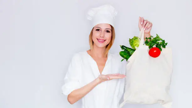 woman in cook uniform holding with different vegetables and showing salad leaves