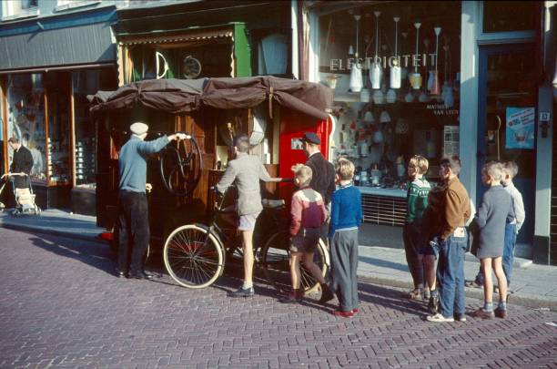 Delft, Netherlands, 1958. A pair of boys inspect an organist as he starts an old jukebox on a street in Delft.