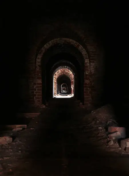 Photo of uninhabited horror horrible long corridor dark with a distant bright light, eerie catacombs with ruinous walls