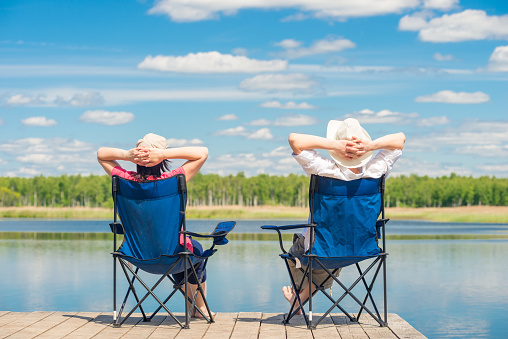 man and woman relax on a pier near a lake sitting on chairs