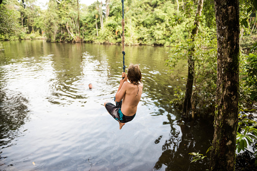 Child swings on rope swing over jungle river