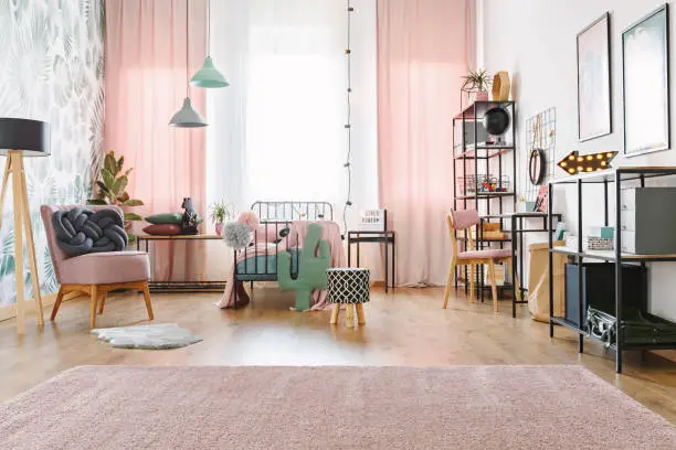 Windows with white and pink curtains in bright kid bedroom interior with lamps, pink chairs and soft carpet