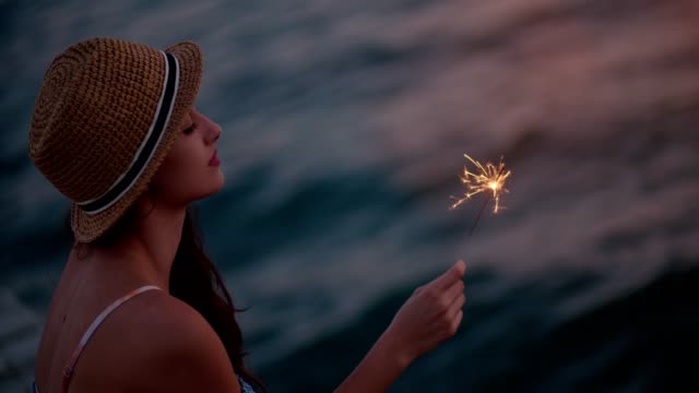 Young woman on summer holidays holding sparklers at the sea