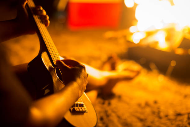 istock A person relaxing while sitting next to a campfire on a beach, playing a guitar 950554594