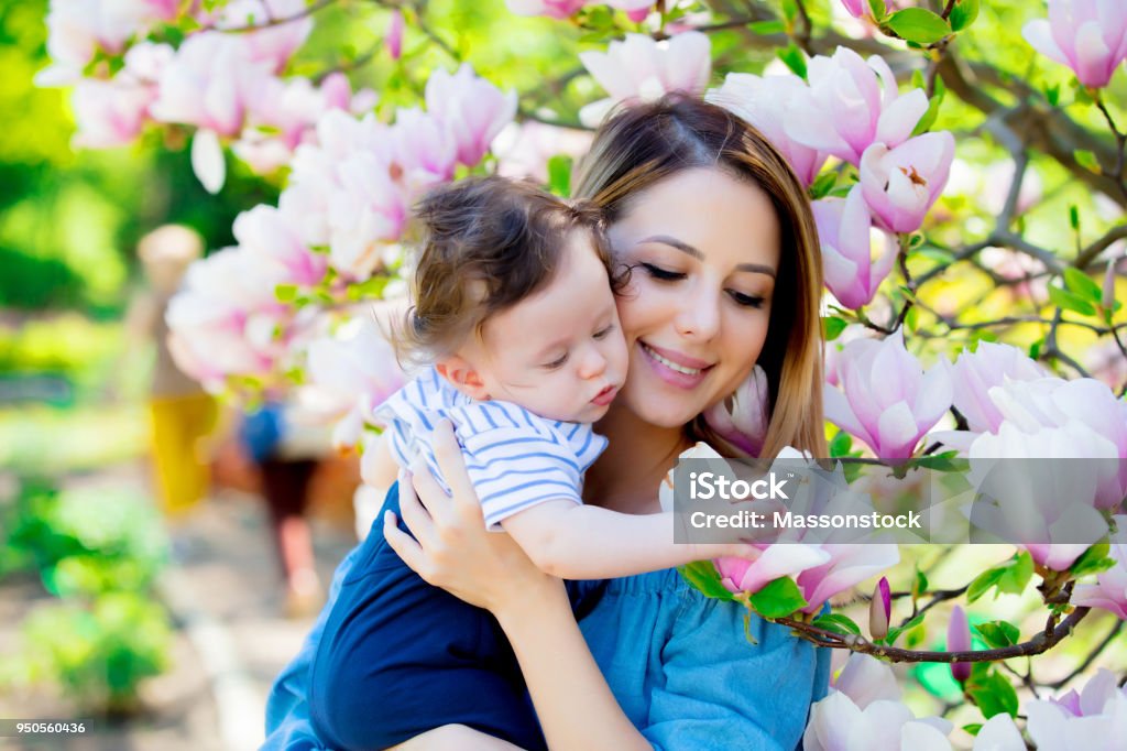 mother and child have a lasure in Magnolia garden Young redhead mother and child have a leisure in springtime flowering Magnolia garden in sunny day. Child Stock Photo